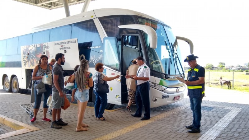 A imagem mostra um fiscal do Daer na rodoviária perto de um ônibus, acompanhando o embarque dos passageiros numa ação de fiscalização da autarquia.