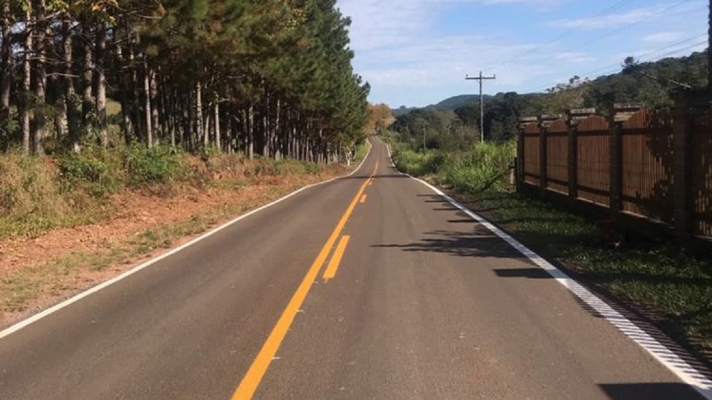 Na foto está a VRS-851 pavimentada com a grande presença de árvores dos dois lados. Está de dia e o céu está com bastante nuvens.