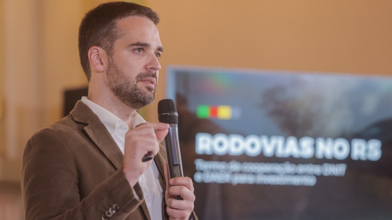 A foto mostra o governador Eduardo Leite falando ao microfone, com um painel com os dizeres "Rodovias no RS" ao fundo.