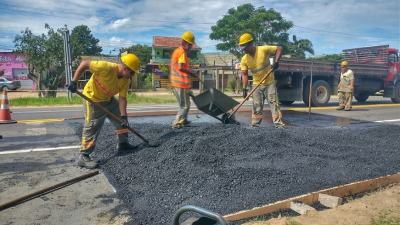 Operários espalham asfalto na pista em obras.
