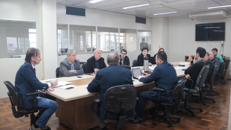 Na foto, secretário Juvir Costella é um homem branco, cabelos escuros, na ponta da mesa.