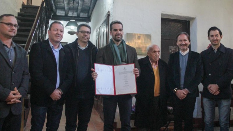 Na foto, o governador é um homem branco, de casaco, cabelos escuros e segura um documento.