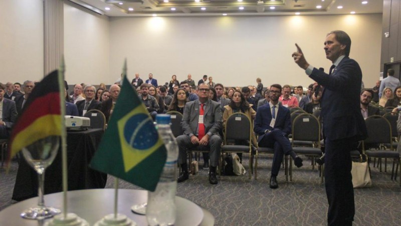Na foto, Juvir Costella é um homem branco, de cabelos escuros, está em pé e usa terno.