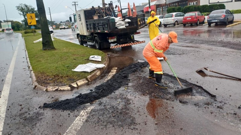A imagem mostra dois homens trabalhando na pista danificada pela chuva e um caminhão estacionado.