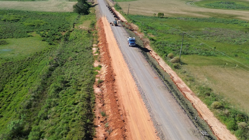 A foto mostra a estrada sendo asfaltada. Tem uma m&aacute;quina e um caminh&atilde;o na obra.