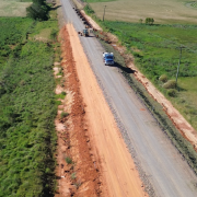 A foto mostra a estrada sendo asfaltada. Tem uma m&aacute;quina e um caminh&atilde;o na obra.